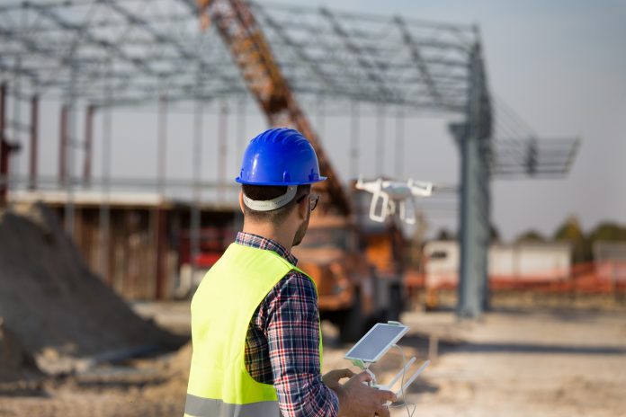 Construction worker with drone at building site Construction and infrastructure, digital/reality capture, drones,