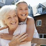Granddaughter Hugging Grandmother On Bench During Visit To Retirement Home