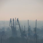 Air pollution at the river port. Portal crane in morning fog in industrial area in city. Bad air quality filled with dust causes of respiratory diseases.