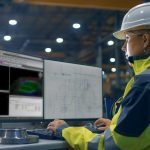 Inside the Heavy Industry Factory Female Industrial Engineer Works on the Personal Computer with Green Mock-up Screen. Secondary Monitor Shows Blueprints.