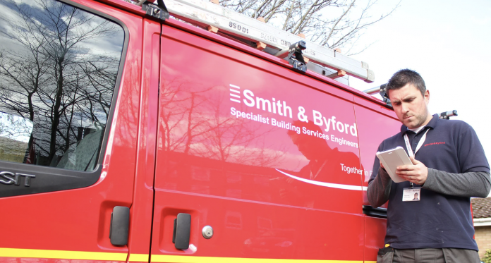 Smith & Byford employee stood next to red company van writing notes