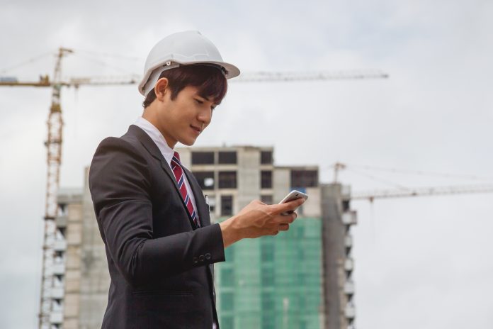 Consultant surveying construction project and sending email report to client via mobile
