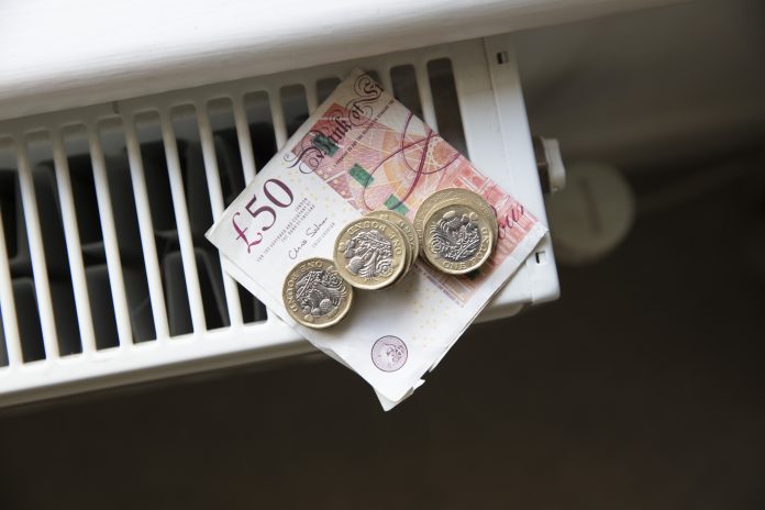 Money on a home radiator heater to represent the cost of living crisis and rising cost of energy and bills