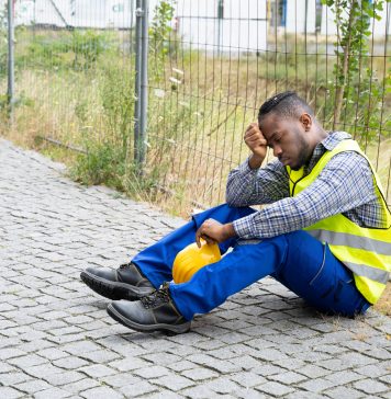 depressed construction worker sat against wire fence