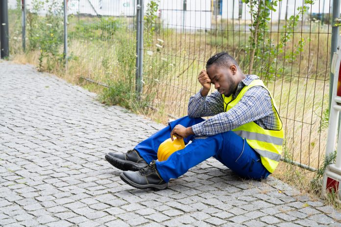dreamstime_xxl_253053560 depressed construction worker sat against wire fence