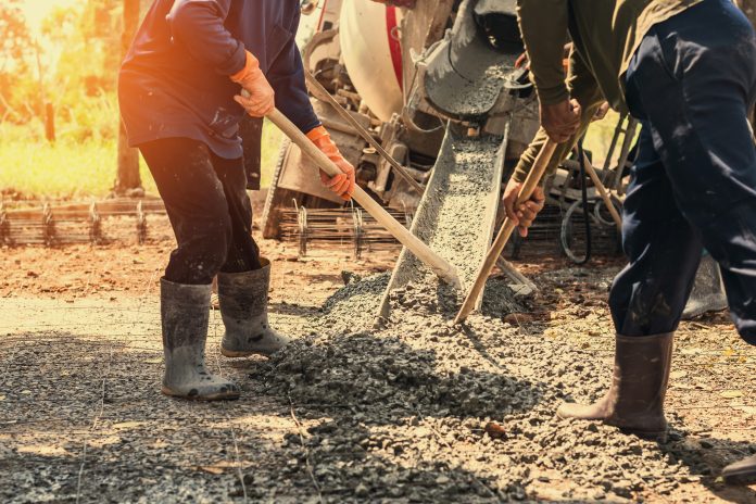 Two construction workers spread concrete mixture with tools, as Reducing carbon in concrete is now the top demand across the building industry, a report from Dodge Construction Network has found