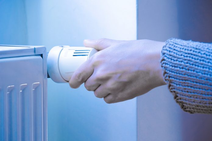 Close Up Shot Of Female Hand Adjusting Thermostatic Radiator Valve Cold Tone following Liz Truss energy price cap announcement