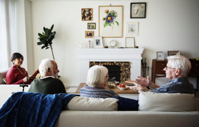 Senior housing residents sat in lounge talking around fireplace