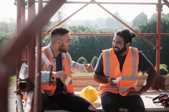 Two young male construction workers enjoy a quiet few minutes, to represent The second annual social value benchmarking report has revealed that over £1bn of economic, social and environmental improvements were made by the UK construction industry last year
