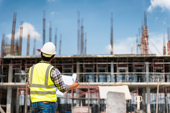 Engineering Consulting People on construction site holding blueprint in his hand. Building inspector. Construction site check drawing design and build contract and business workflow of new building