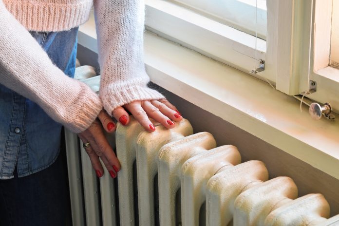 Home central heating system, woman`s hands on an old and robust metal radiator