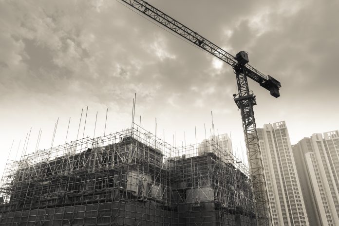 black and white image of crane at construction site, high rise buildings
