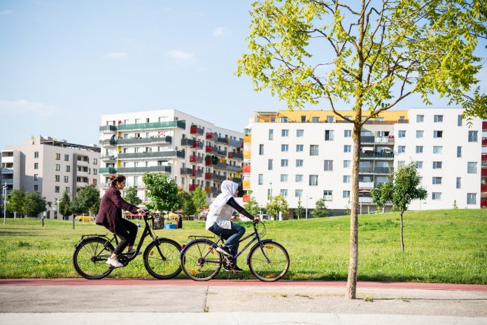 two people cycling in front of sustainable development buildings surrounded by greenery