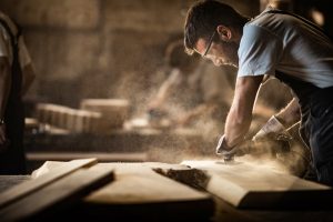 Manual worker using sander while working on a wood in carpentry workshop.