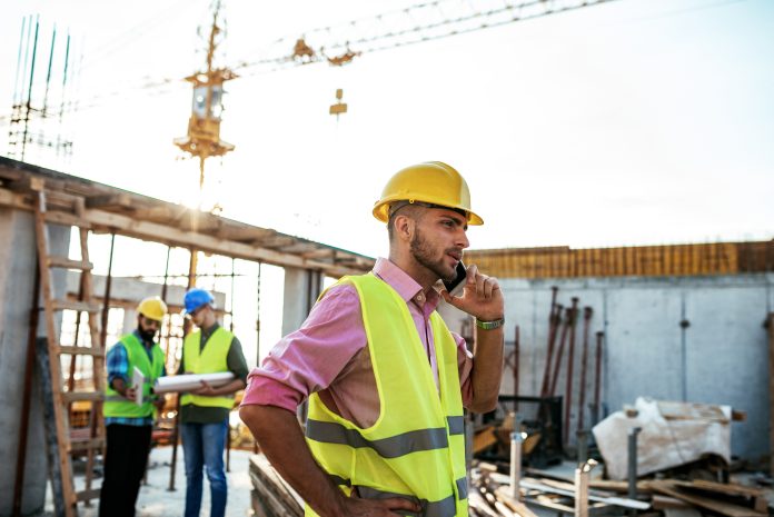 Construction industry concept - architects and engineers discussing work progress between concrete walls, scaffolds and cranes.
