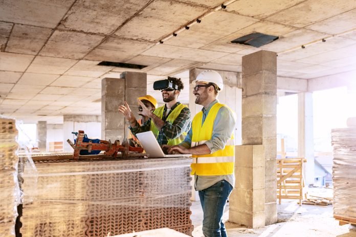 Photo of young male team of business people in group, architect and engineer on construction site checking documents and business workflow using the virtual reality headset and laptop computer in new startup office.