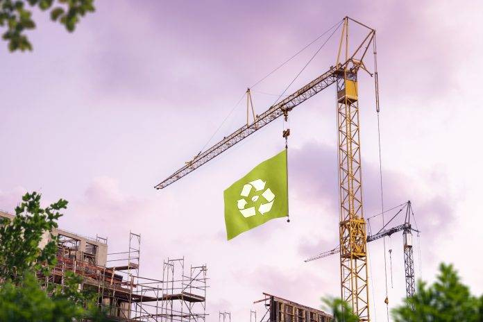 Sustainable building. A construction site with a crane hoisting a green flag with a recycling symbol.