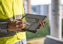What are the benefits of using a purpose-made solution for construction project documentation? Engineer comparing the projects on his tablet with the actual work done on the site. Man working in the construction industry.