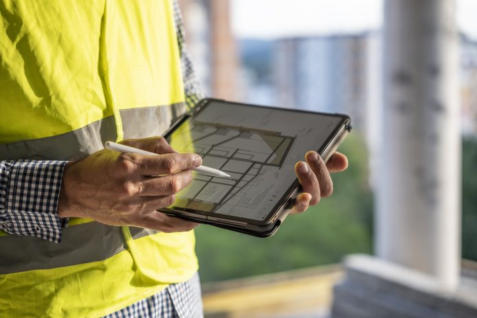 Civil engineer working with tablet on construction site, checking the work progress. Engineer comparing the projects on his tablet with the actual work done on the site. Man working in the construction industry.