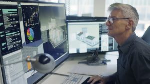 Stock image of a mature man working on a CAD design of an Eco house with associated data on screen.