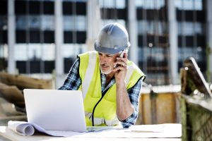 Male architect using mobile phone and laptop at construction site