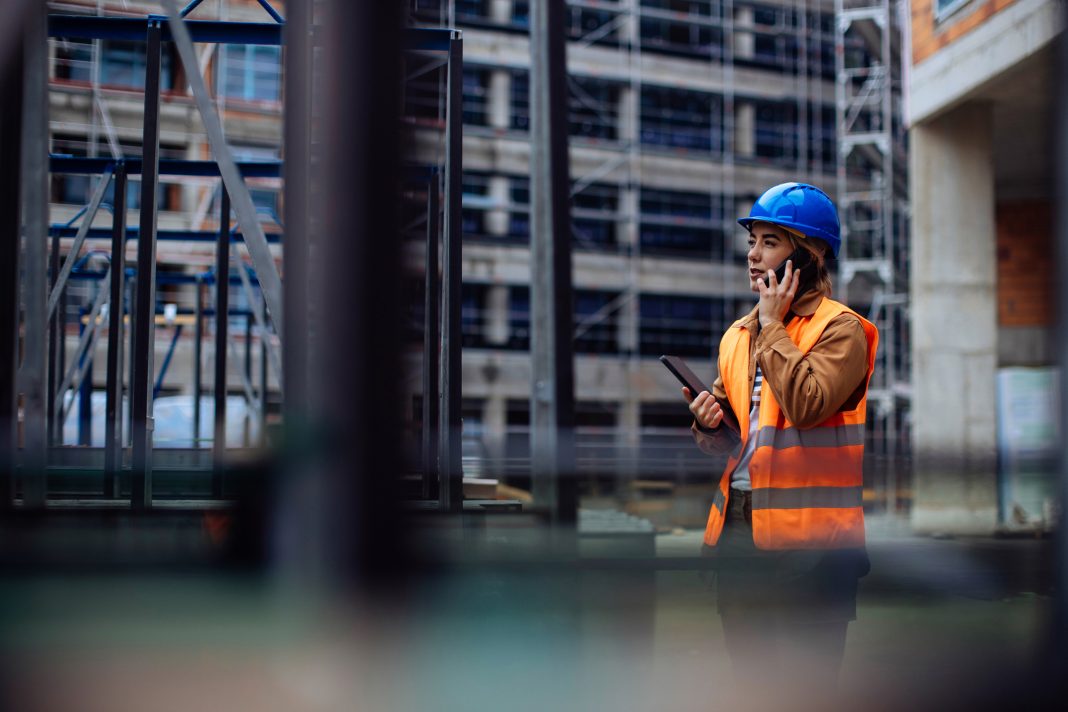 Young female worker having a phone call at a construction site, representing building a resilient construction business