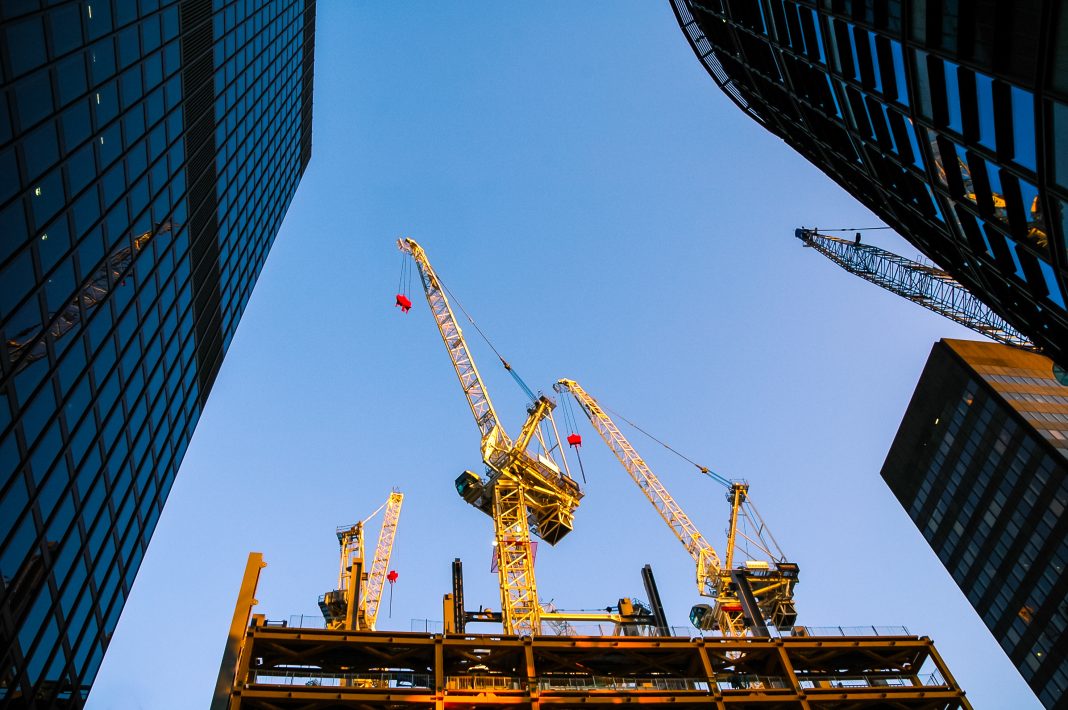 A crane sits in between two high rise buildings in downtown London, to represent the volume of new office refurbishment schemes