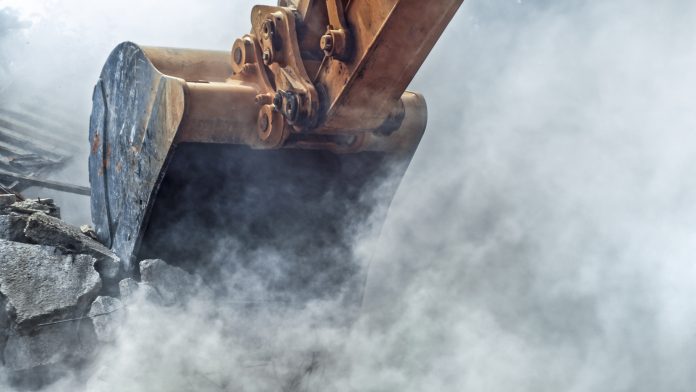 Diesel-free construction sites by 2035 Excavator demolishing wall of an old house.