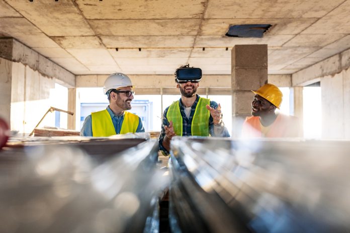 Photo of young male team of business people in group, architect and engineer on construction site checking documents and business workflow using the virtual reality headset in unmade new startup office.