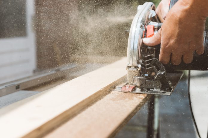 Carpenter using circular power saw for cutting wood, home improvement, do it yourself (DIY) and construction works concept, action shot, representing the risk of wood dust exposure