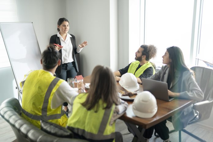 Aldermore launch new construction finance team Businesswoman is talking about new project in the meeting room. Her team is sitting around a table and listening their manager carrefully.