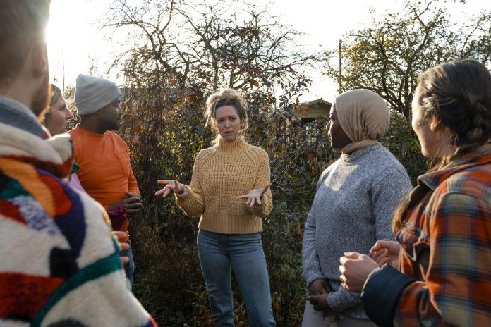 A multiracial group of volunteers wearing warm casual clothing and accessories on a sunny cold winters day. They are talking before they start working on a community farm, planting trees and performing other tasks, representing the value of community engagement