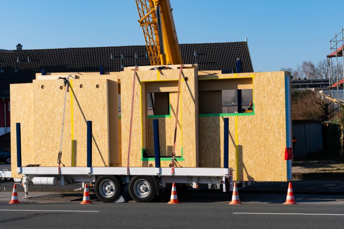 Ready for unloading panels of a wooden prefabricated house. Crane boom at the back. Car trailer.. representing the news that modular housebuilder Ilke Homes is up for sale