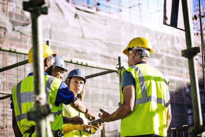 Team of architects and workers discussing over digital tablet at construction site, representing the growing role of accreditation in the construction industry