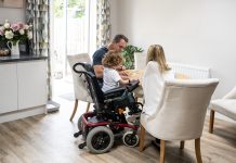 Disability housing inquiry from Levelling Up Committee now seeking evidence 6 year old boy with muscular dystrophy, sitting at dining table with mother and father, playing a game, quality time with family, representing the disability housing inquiry