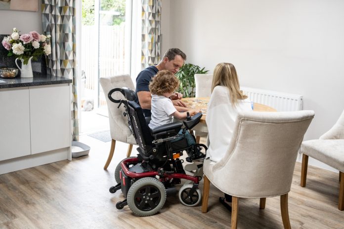 6 year old boy with muscular dystrophy, sitting at dining table with mother and father, playing a game, quality time with family, representing the disability housing inquiry