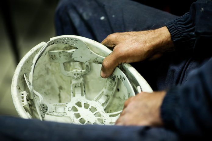 Details with the hands of a factory worker holding his dirty protective helmet, representing Ilke homes falling into administration