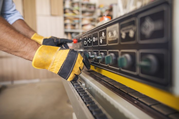 Unrecognizable male hands with work gloves on setting up large industrial woodworking machine, representing the wood panel engineer that was fined