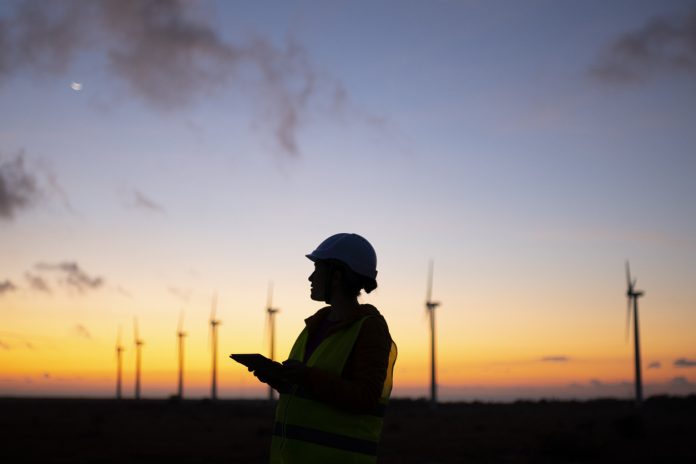 Electrical engineer working for the energy industry, supervising the condition of the Electrical Power Equipment in a wind turbines farm power station at night, representing the green energy revolution
