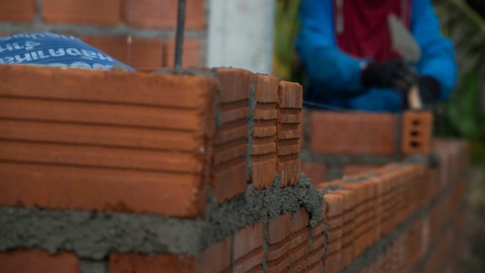 Construction project starts continue to slide on downhill trajectory, reports Glenigan Professional construction worker laying bricks and building