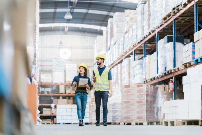Male and female workers discussing over stock checklist in warehouse. Multi-ethnic colleagues are working together at distribution warehouse, walking by the racks and looking the stock levels, representing Click Aylesford
