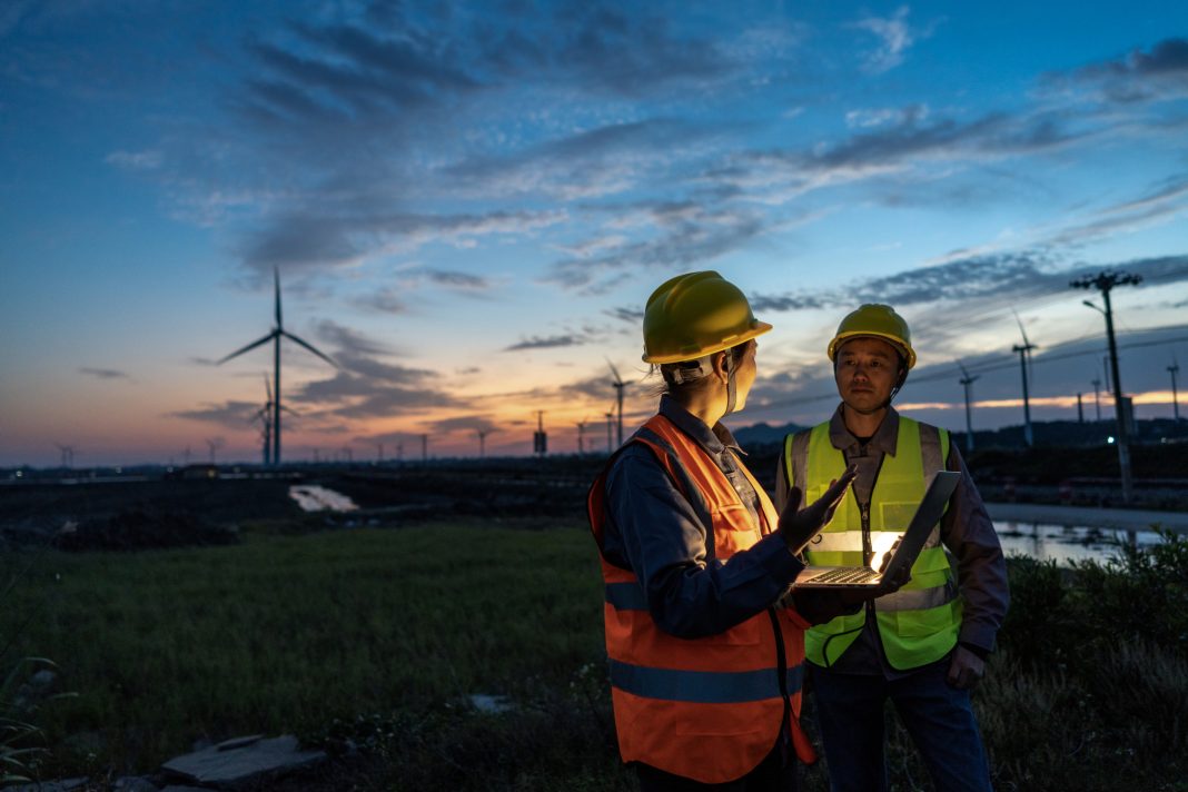 Two engineers hold computers at the wind power airport to discuss data Two engineers hold computers at the wind power airport to discuss data