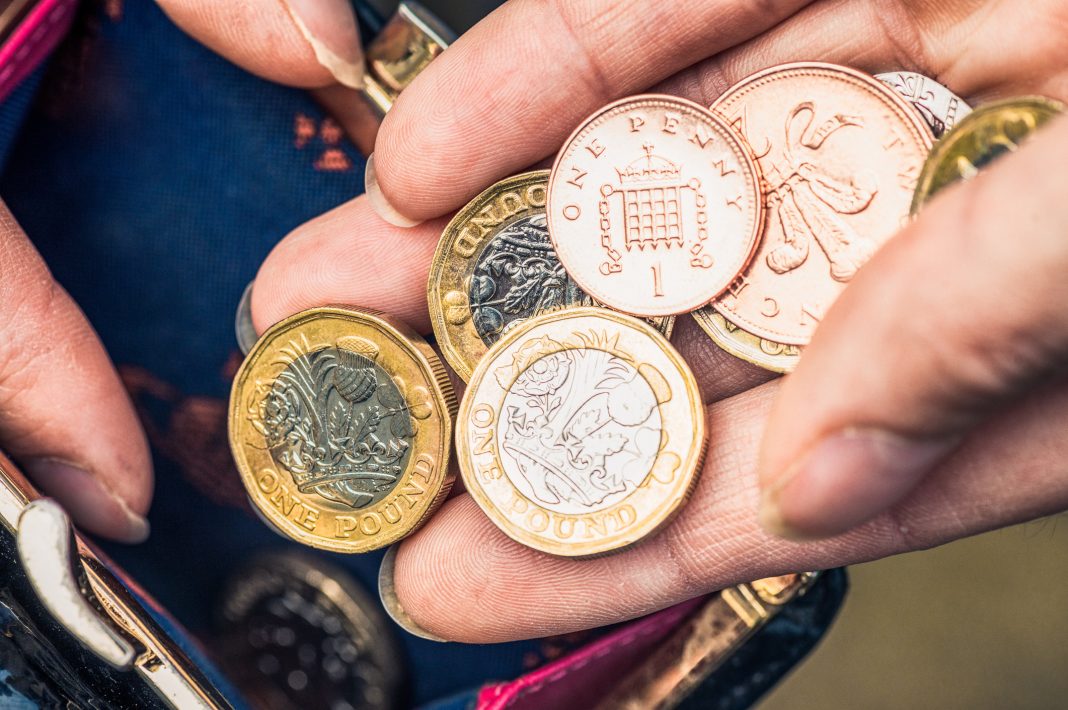 Close-up of a woman's hand holding one pound coins and other change from her purse, representing the inflation rate drop