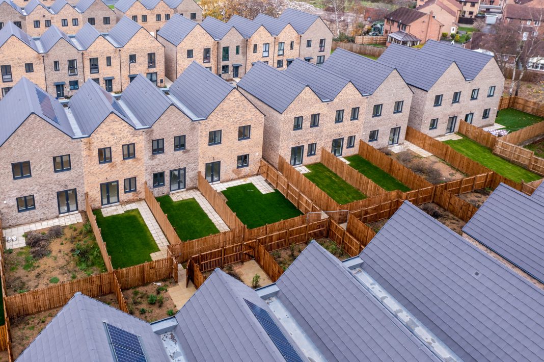 Aerial view of rows of generic new build modular terraced houses with energy efficient rooftop solar panels in the UK with characterless design for first time buyers