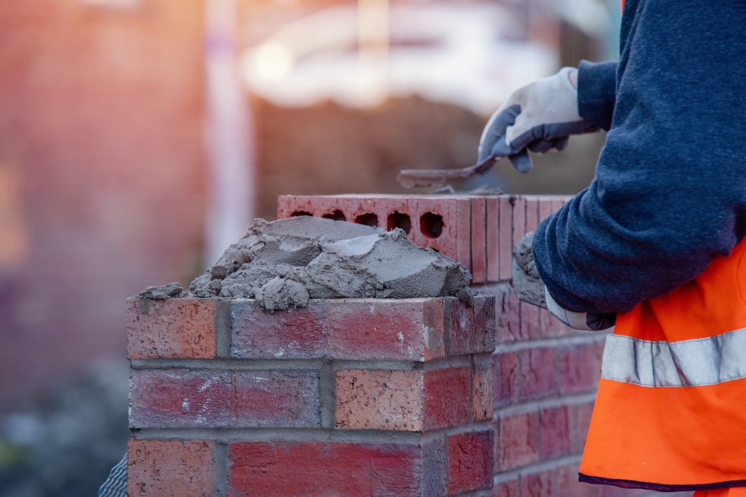 Close up of industrial bricklayer laying bricks on cement mix on construction site, representing vacancies in construction trades