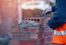 Skills shortage reaches 140,000 vacancies in construction trades in the UK Close up of industrial bricklayer laying bricks on cement mix on construction site, representing vacancies in construction trades