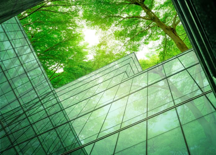 Less talk, more action: Why the industry needs to work together to tackle carbon net zero Eco-friendly building in the modern city. Sustainable glass office building with tree for reducing heat and carbon dioxide. Office building with green environment. Corporate building reduce CO2.