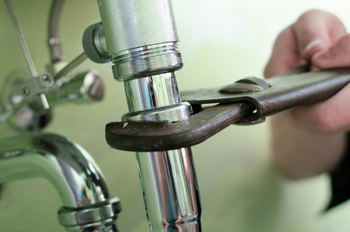 Plumber using a wrench to tighten a siphon under a sink, representing Hampshire plumber gets suspended sentence