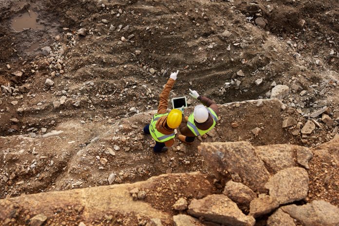 Improving safety, efficiency and cost savings with total productive maintenance Top view shot of two industrial workers wearing reflective jackets standing on mining worksite outdoors using digital tablet, copy space, representing total productive maintenance
