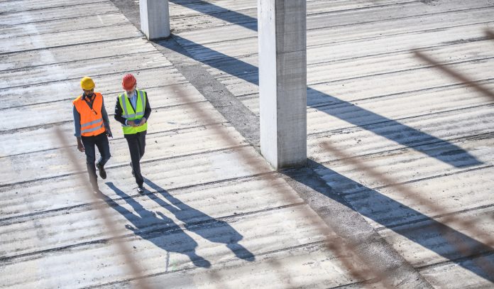 Elevated view through defocused rebar in foreground of construction site foreman and manager walking and talking.